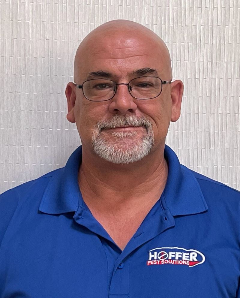 Man with glasses and goatee stands smiling slightly.