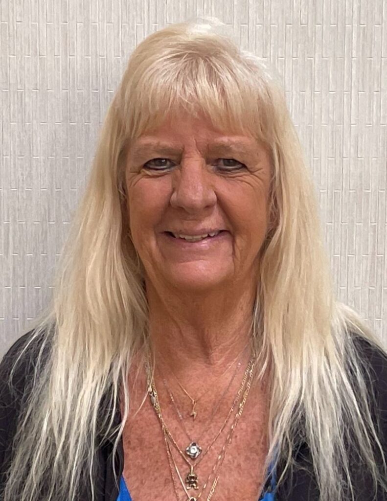 Smiling older woman with long blonde hair stands.