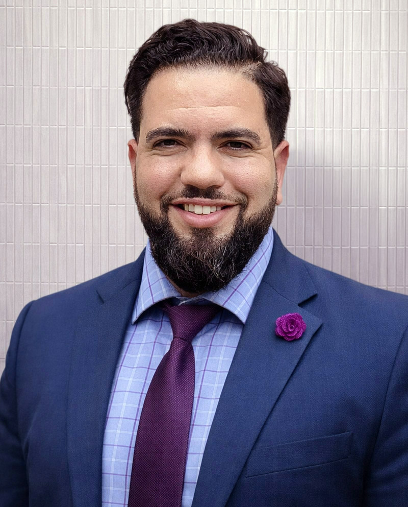Man in blue suit and purple tie smiling.