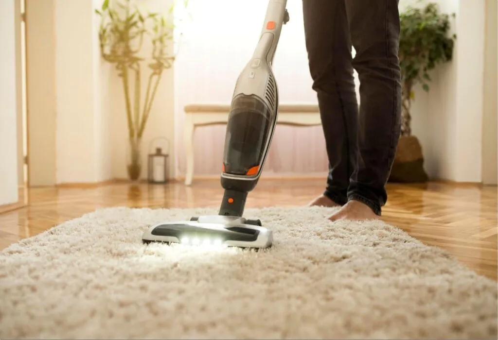 Person vacuums carpet barefoot on a light-colored rug.