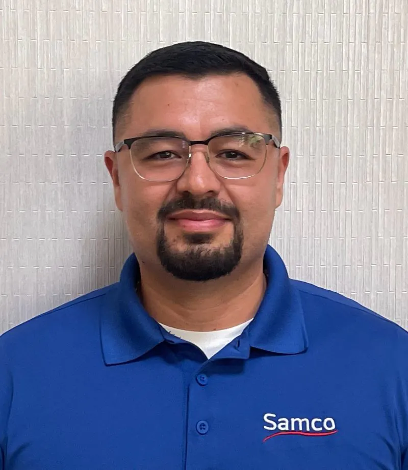 Man with glasses and beard smiles in blue Samco polo.