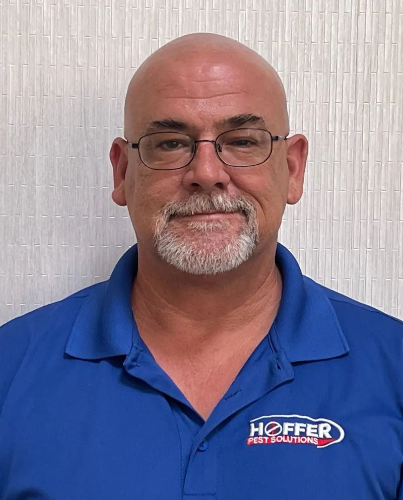 Man with glasses and goatee stands smiling slightly.