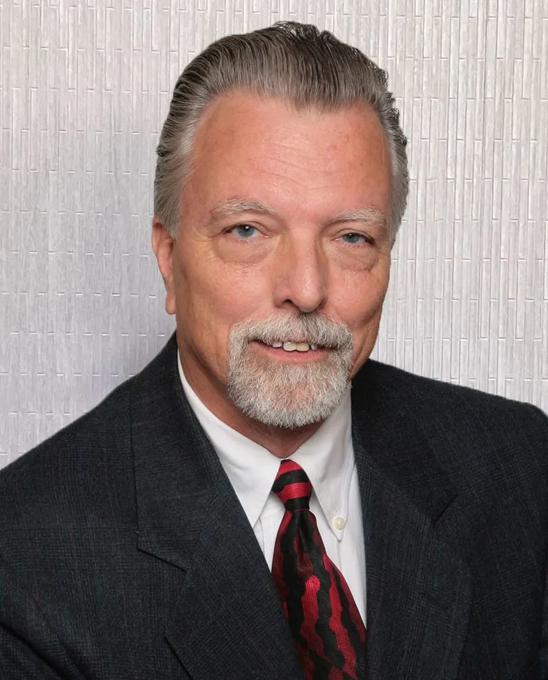 Middle-aged man with gray hair smiling in a suit.