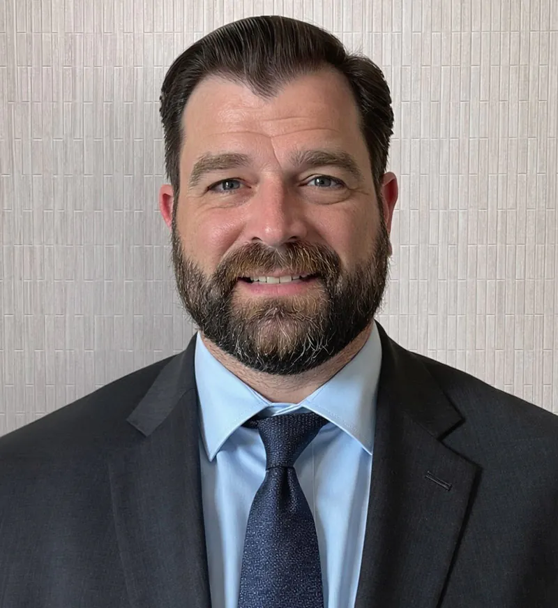 Man with dark hair and beard smiles.